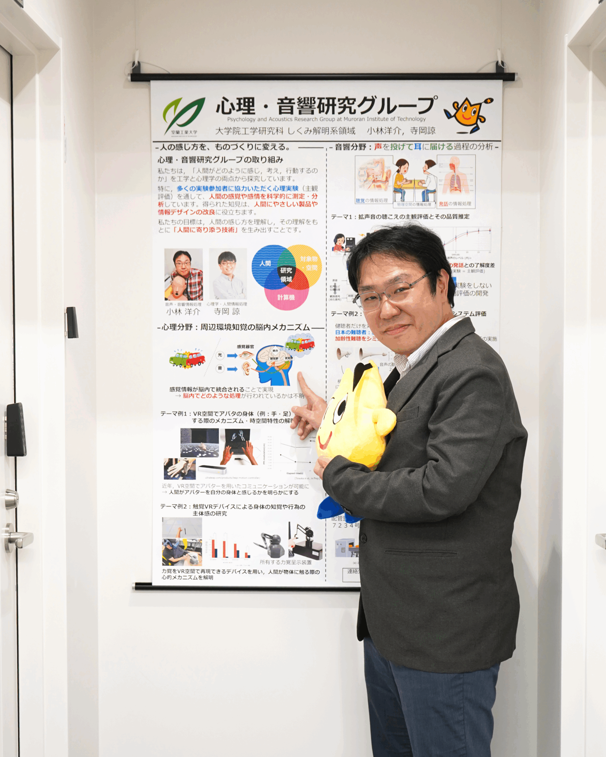 ポスターレールにポスターを吊り下げて指さしている小林洋介先生